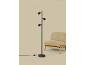 Lampadaire noir avec trois spots orientables à côté d'un fauteuil beige.