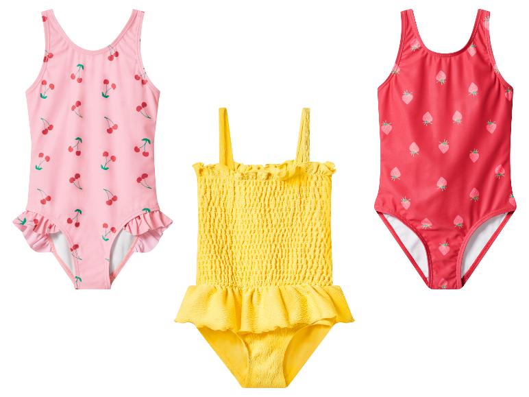 Trois maillots de bain pour enfants: rose à cerises, jaune à volants et rouge à fraises.