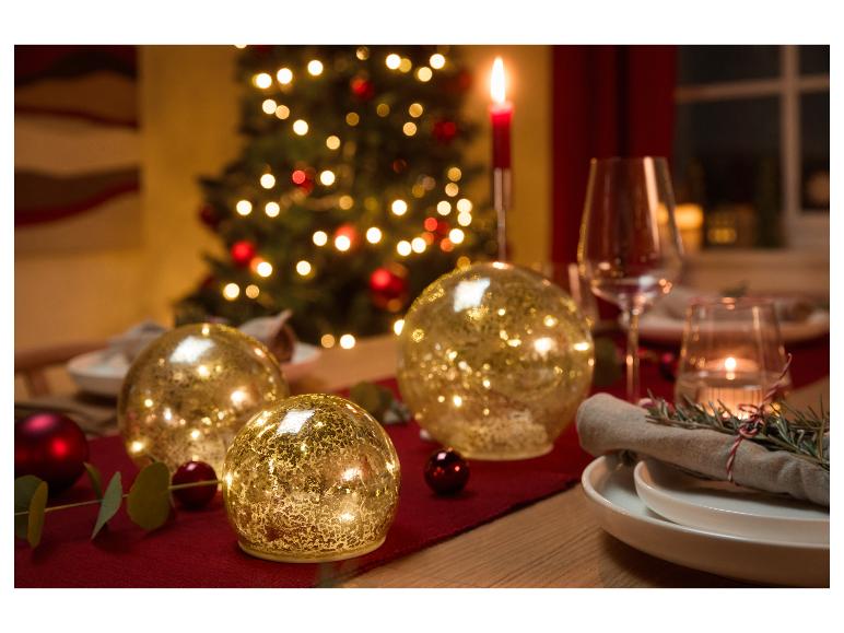 Table de Noël décorée d'orbes dorés lumineux, de bougies et d'un sapin de Noël en arrière-plan.