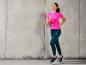 Une femme portant des vêtements de sport, dont un t-shirt rose et un legging bleu, court.