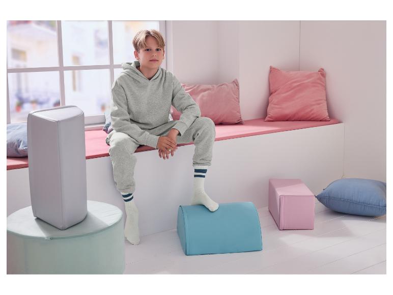 Un garçon est assis sur un banc de fenêtre, entouré de coussins et de poufs colorés.