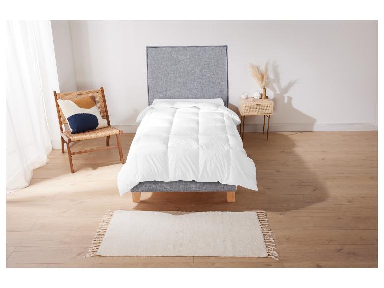 Une couette blanche sur un cadre de lit gris avec un tapis et une chaise.