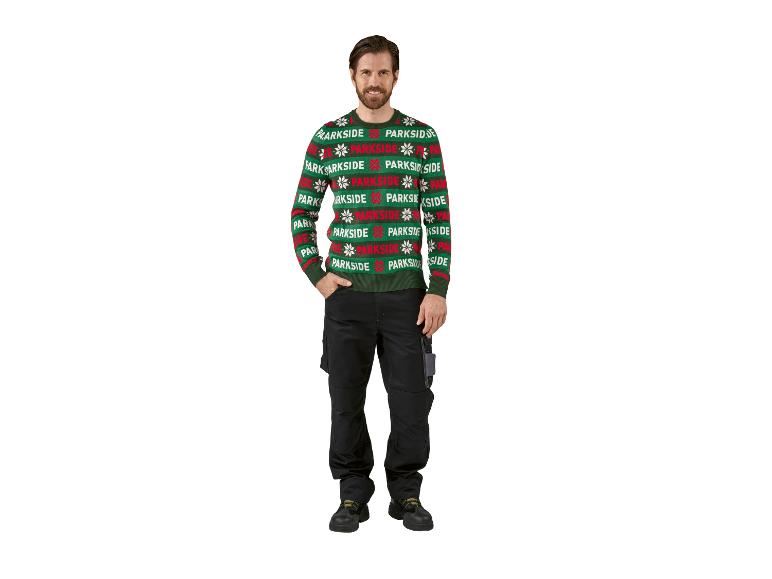 Homme souriant portant un pull vert festif et un pantalon noir.