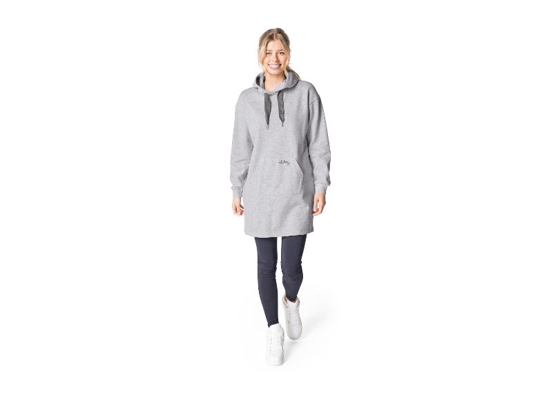 Une femme porte un sweat à capuche gris avec 'Mickey' et des baskets blanches.