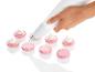 Une main décorant des macarons roses avec une douille.