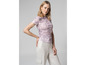 Une femme porte un t-shirt rose avec un motif abstrait et un pantalon blanc.