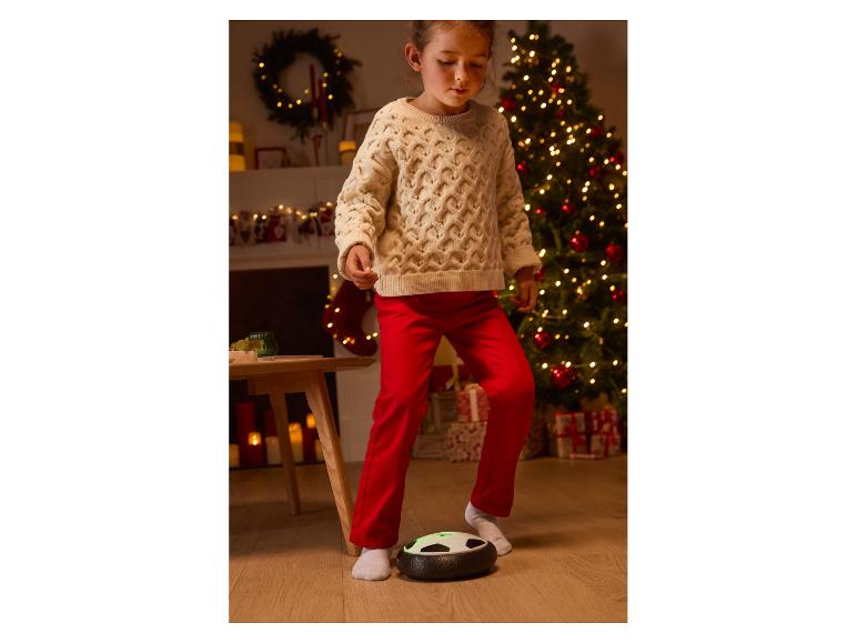 Fille jouant au football avec un ballon flottant dans un décor de Noël.