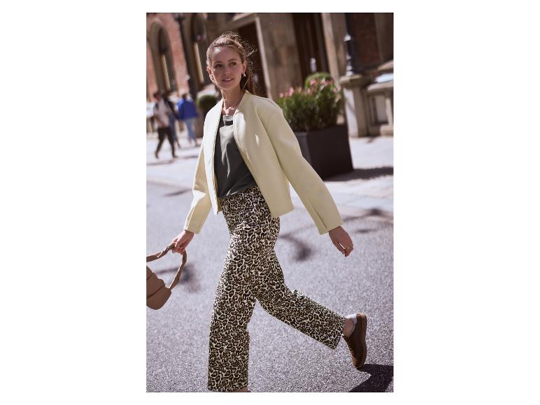 Femme marchant dans la rue, vêtue d'un pantalon léopard et d'une veste crème.