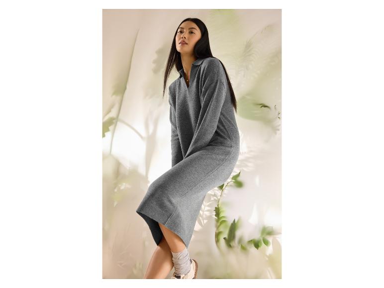Femme en robe pull grise et baskets blanches, assise sur un fond clair avec des plantes.