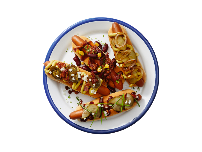 Quatre hot-dogs avec différentes garnitures comme du chili, des oignons, des cornichons et de la moutarde sur une assiette.