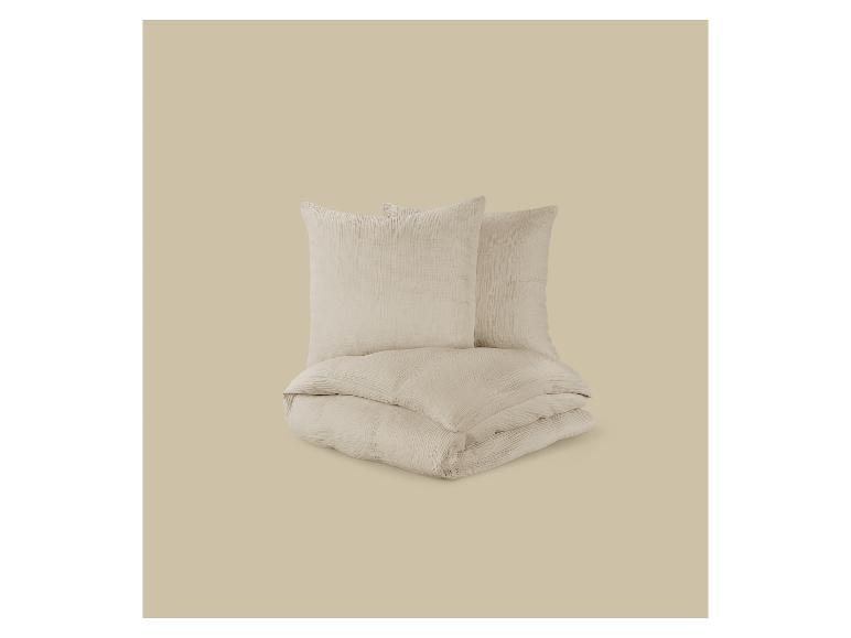 Parure de lit beige clair avec deux oreillers et une couette pliée.