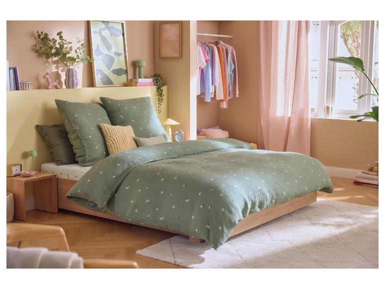 Chambre avec un lit, une housse de couette florale verte et des oreillers, et une petite armoire.