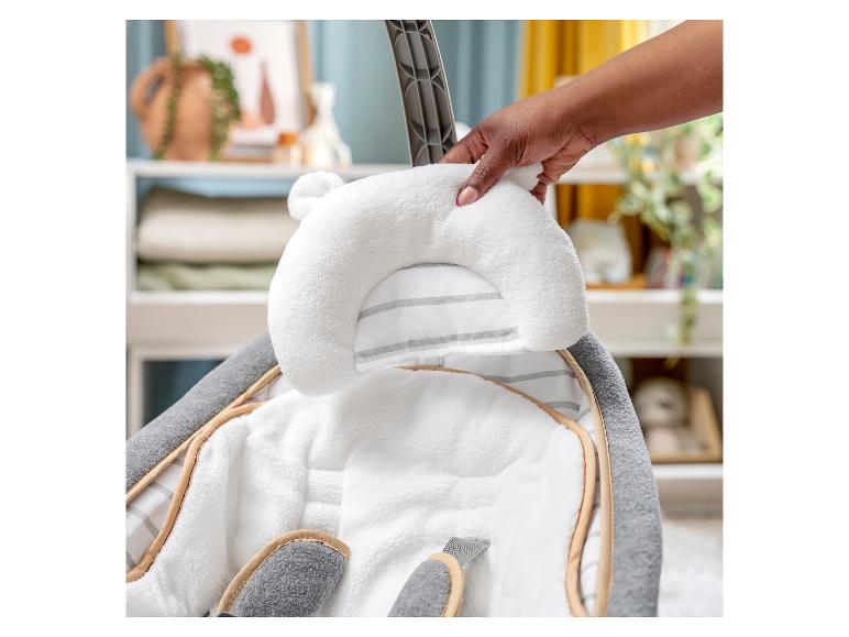 Main de femme plaçant un coussin blanc doux avec des oreilles dans un transat bébé.