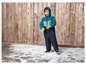 Un enfant dans une combinaison d'hiver bleue se tient sur un sol en bois avec de la neige artificielle.