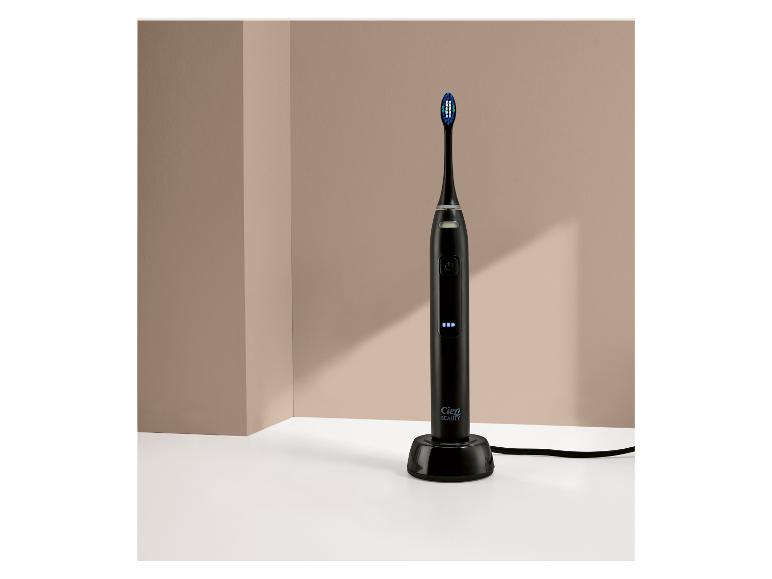 Une brosse à dents électrique noire avec des poils bleus et des voyants lumineux, sur une base de chargement.