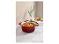 Cocotte rouge remplie de ragoût sur un comptoir en marbre avec une manique