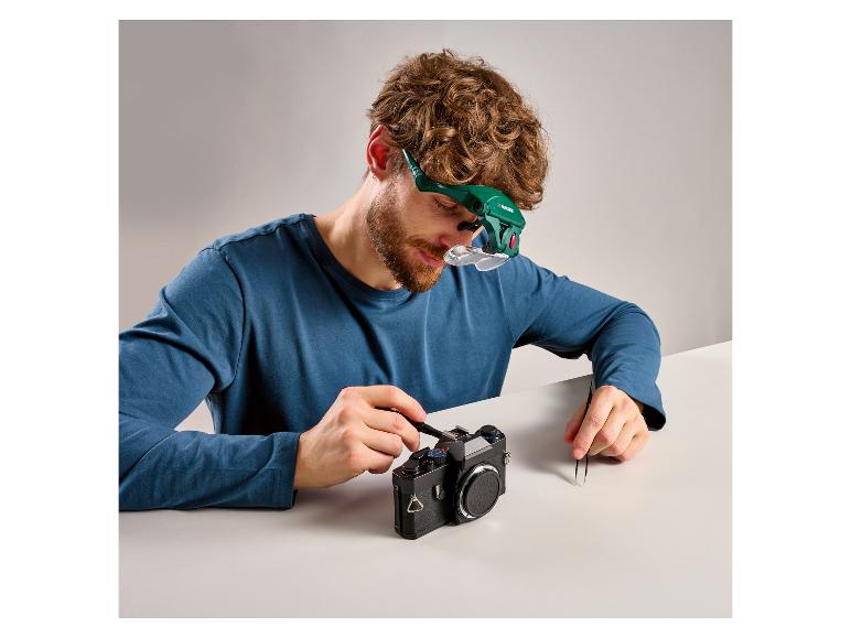 Homme répare un appareil photo avec une loupe et des outils.