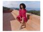 Femme en robe fuchsia et chaussures confortables assise sur une terrasse avec vue mer.
