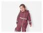 Petite fille souriante portant un ensemble imperméable bordeaux.