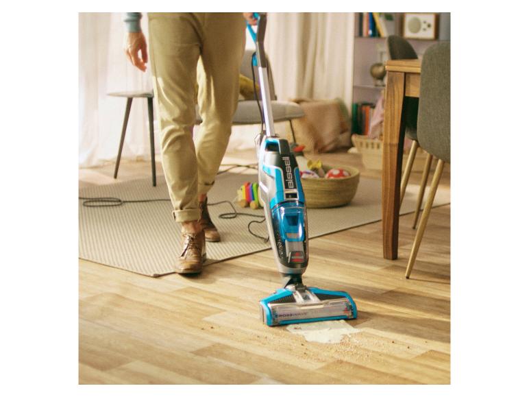 Un homme utilisant un aspirateur balai Bissell Crosswave sur un plancher de bois.