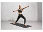Une femme en tenue de sport noire fait du yoga sur un tapis noir.