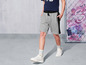 Un modèle porte un short gris avec des accents noirs et des baskets blanches.