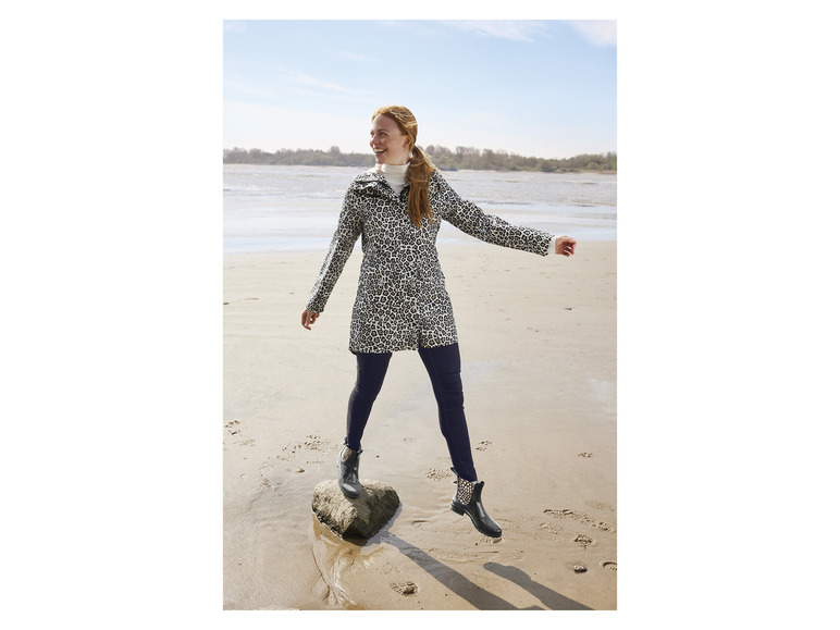 Une femme porte un blouson léopard et des bottes de pluie noires sur la plage.