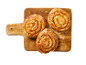 Trois escargots à la cannelle sur une planche à découper en bois.
