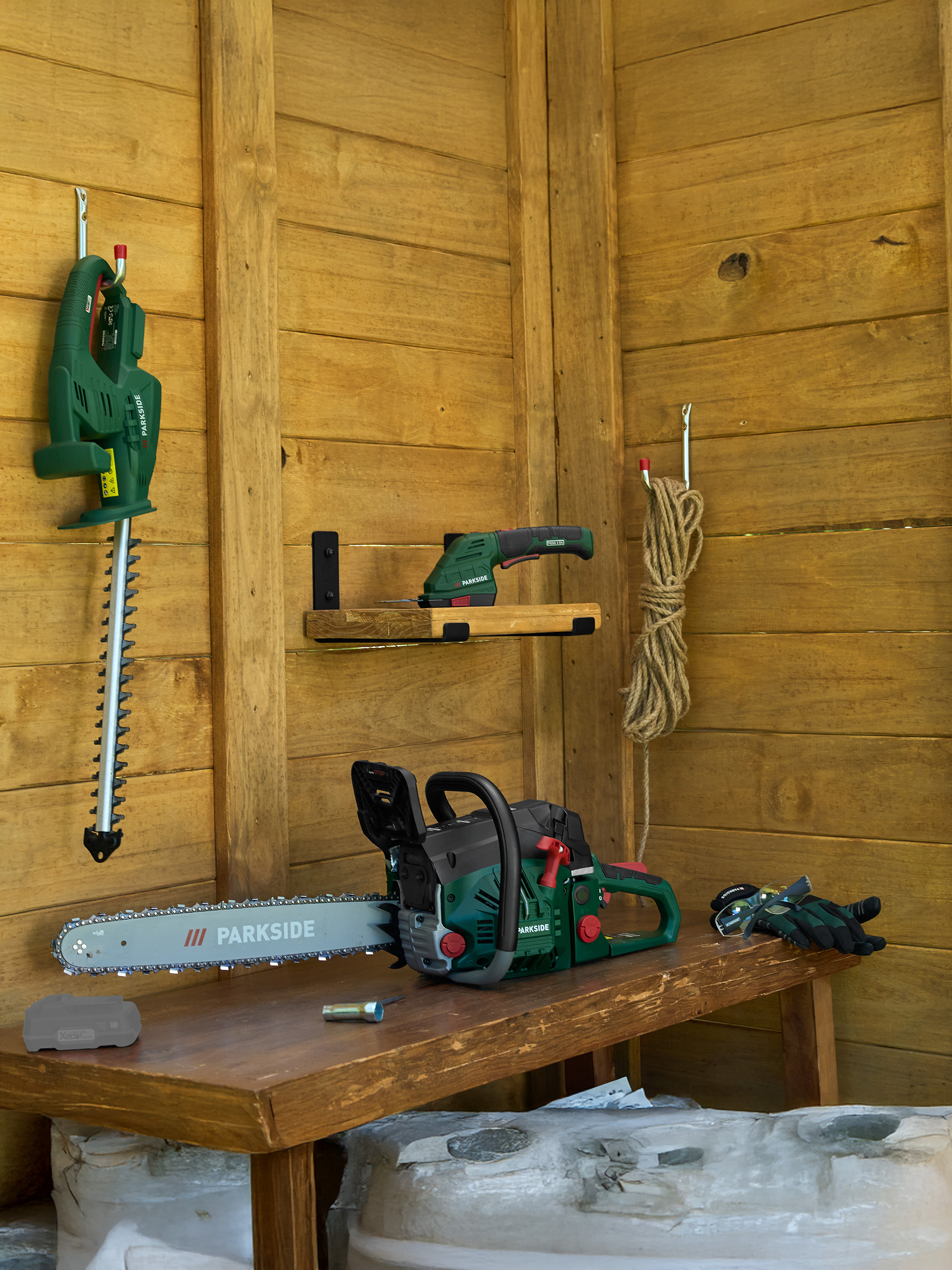 Tronçonneuse, taille-haie et cisaille de jardin dans un abri en bois avec des outils de jardinage.