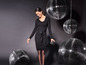 Une femme en robe noire pose devant des boules à facettes.