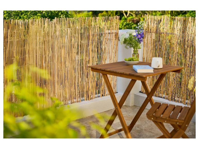 Balcon avec clôture en bambou, table et chaise en bois, fleurs et livre.