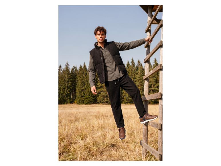 Homme en jean, gilet et baskets marron sur une échelle en bois dans la nature.