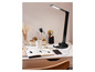 Une lampe de bureau noire sur un bureau avec un carnet, des stylos, un téléphone et une tasse de café.