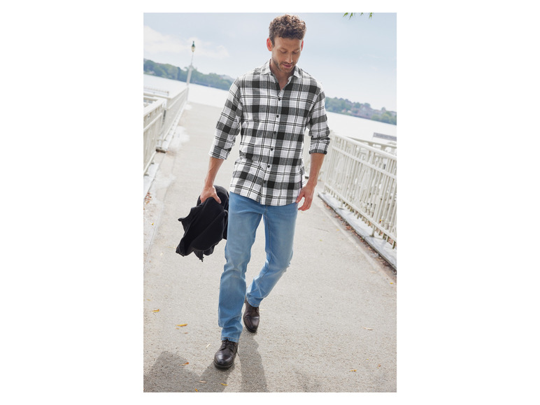 Un homme en chemise à carreaux et en jean marche sur une jetée.
