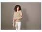Femme portant un pull beige et un pantalon blanc.