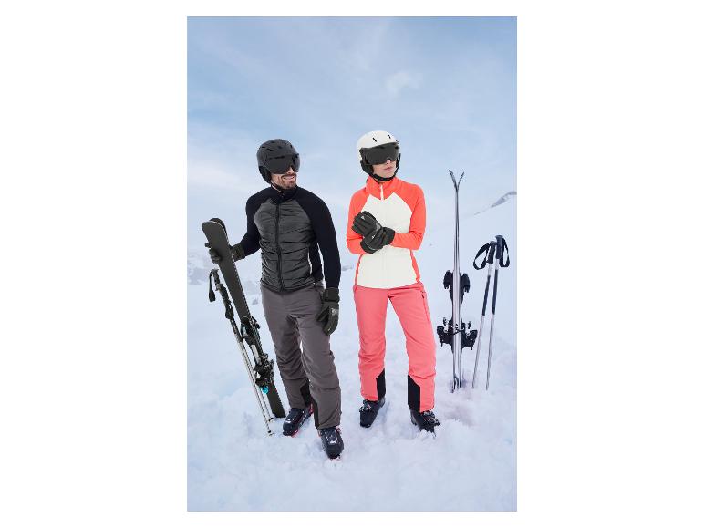 Un homme et une femme en tenue de ski se tiennent dans la neige avec des skis et des bâtons.