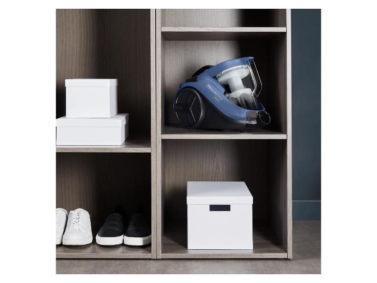 Un aspirateur Rowenta, des chaussures et des boîtes de rangement dans une armoire en bois.