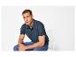 Homme en polo bleu marine et jean assis sur une chaise blanche