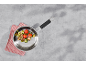 Poêle avec tomates, courgettes et champignons sautés sur une surface grise.