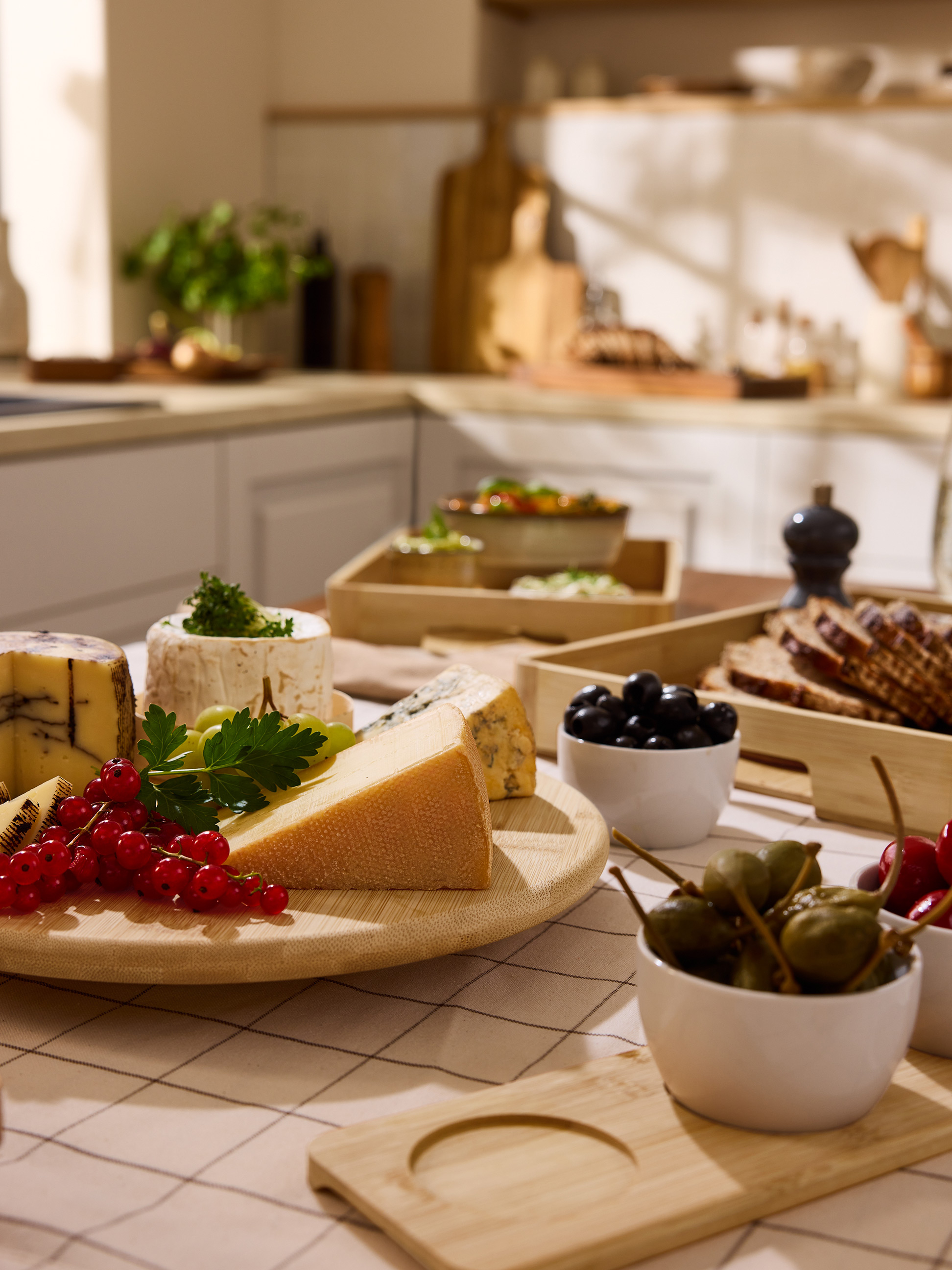 Plateau de fromages avec baies, olives et pain, sur une table de cuisine.