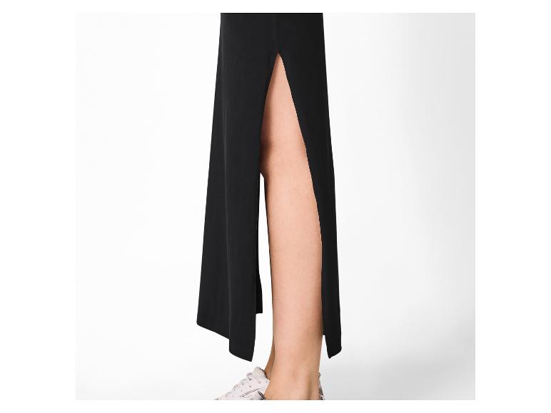 Jupe longue noire fendue, jambes visibles et chaussures de sport blanches.