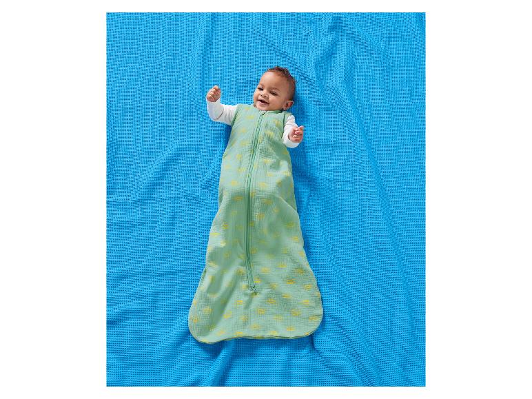 Bébé heureux dans une gigoteuse verte à motifs de soleil sur une couverture bleue.