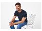Homme en t-shirt bleu foncé et jean assis sur une chaise, souriant.