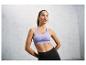 Une femme porte un soutien-gorge de sport violet et un legging noir.