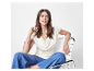 Modèle en blouse blanche et jeans bleus assise sur une chaise blanche.
