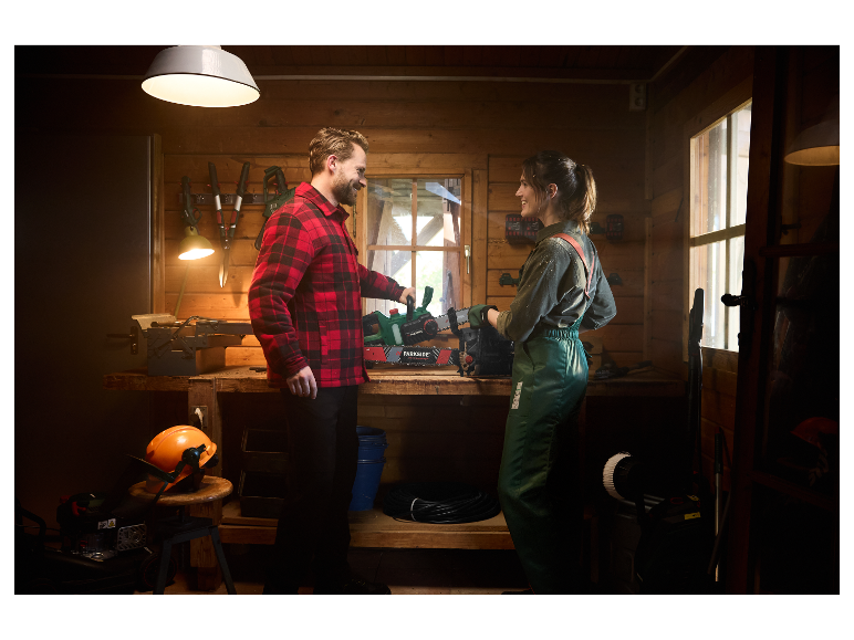 Un couple regarde une tronçonneuse Parkside dans un atelier en bois.