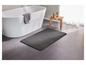 Un tapis de bain gris dans une salle de bain avec une baignoire et un tabouret en bois.