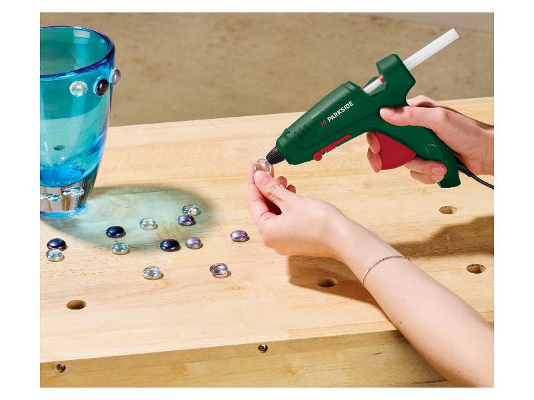 Personne utilisant un pistolet à colle Parkside pour fixer des pierres décoratives sur un vase bleu.
