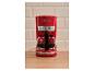 Cafetière rouge avec une carafe en verre remplie de café, sur un comptoir en bois.
