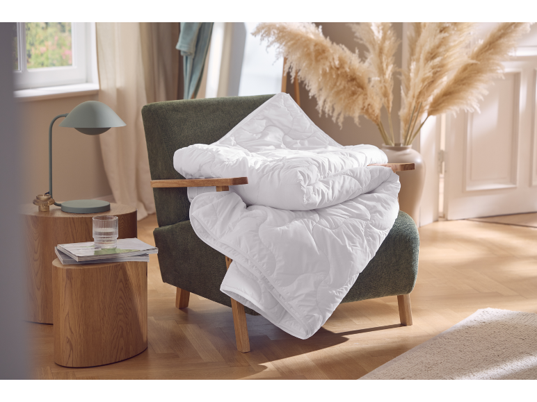 Couette blanche sur un fauteuil, table d'appoint en bois avec lampe et verre.